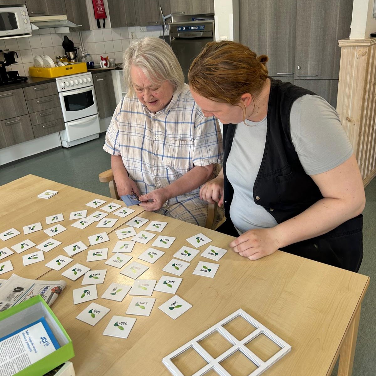 Vanha nainen pelaa muistikorttipeliä nuoren hoitajan kanssa. 