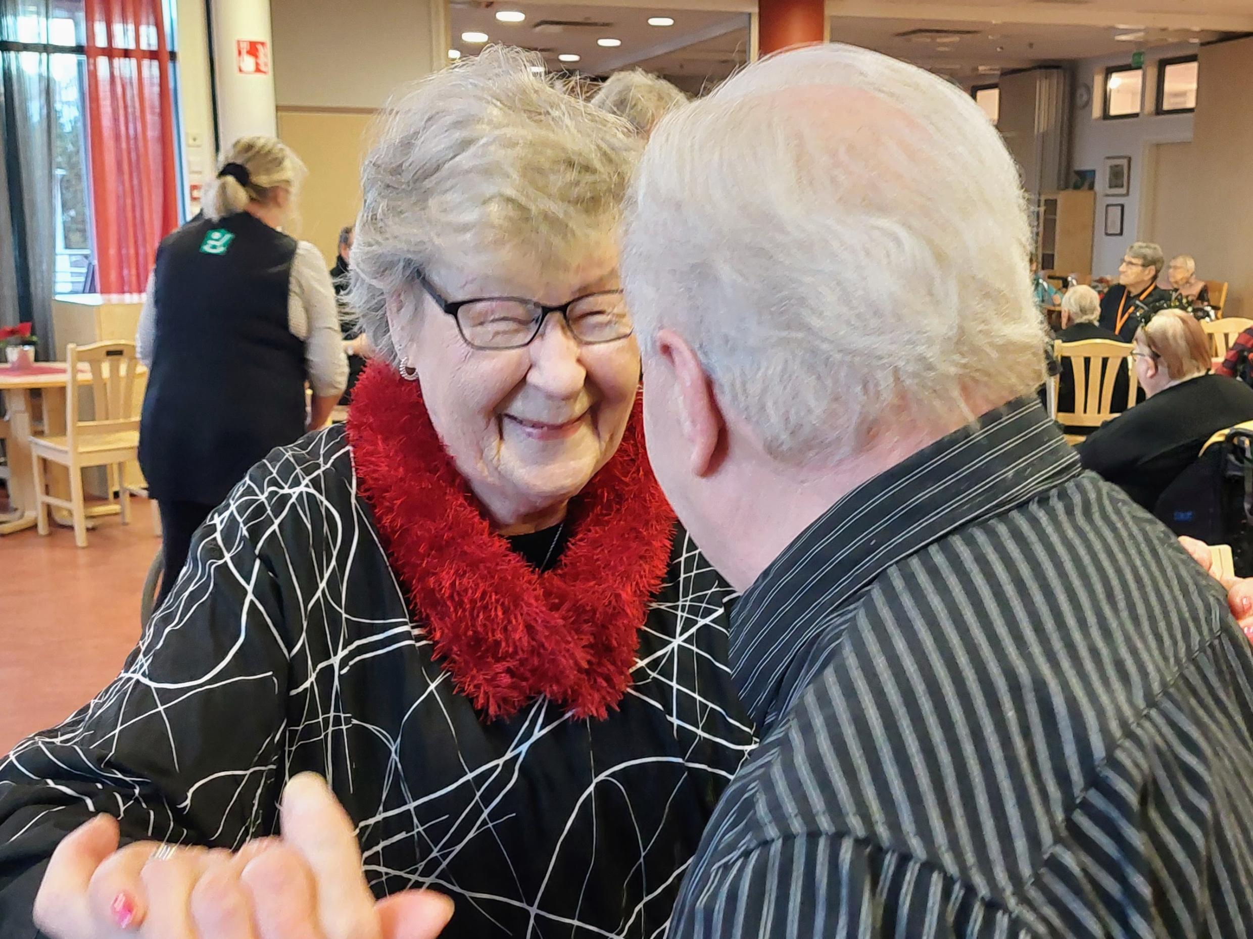 Vanhuspari tanssii. Nainen hymyilee kameralle